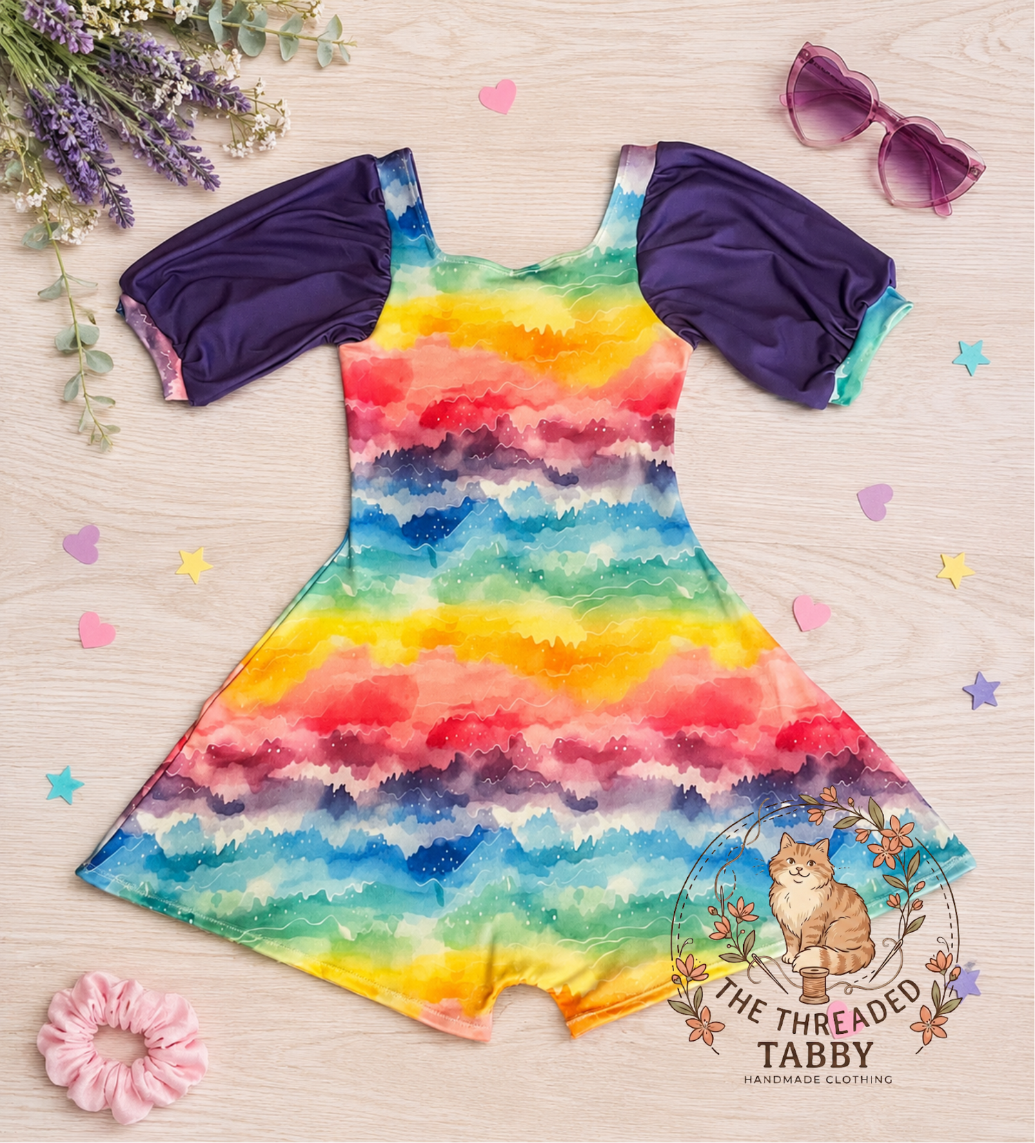 Colorful rainbow dress with matching top and accessories on a wooden surface with 'The Threaded Tabby' branding.